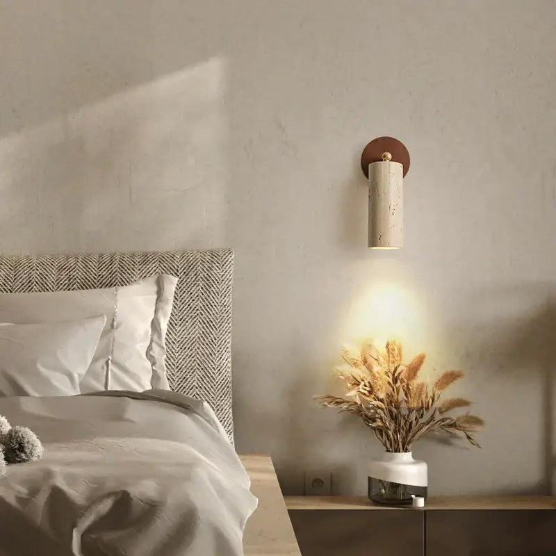 A modern beige stone and bronze cylindrical wall light fixture with a textured body and circular copper backplate