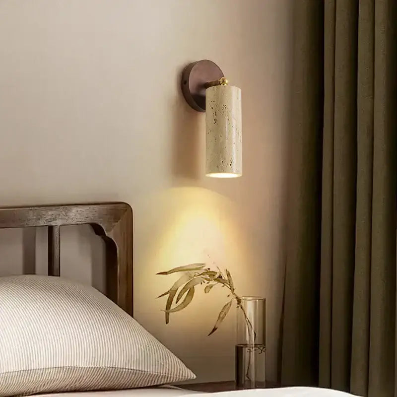 Modern beige stone and bronze wall light fixture with a cylindrical body and warm light for bedroom use