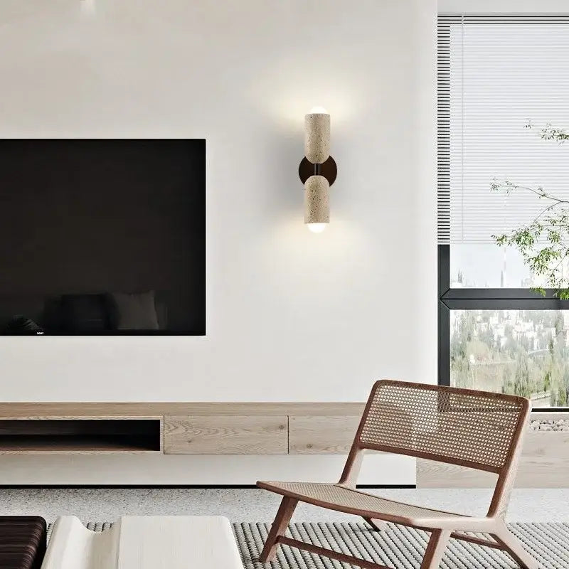 Modern beige stone and wood wall light fixture with cylindrical textured stone finish and dark bronze accents for bedroom use