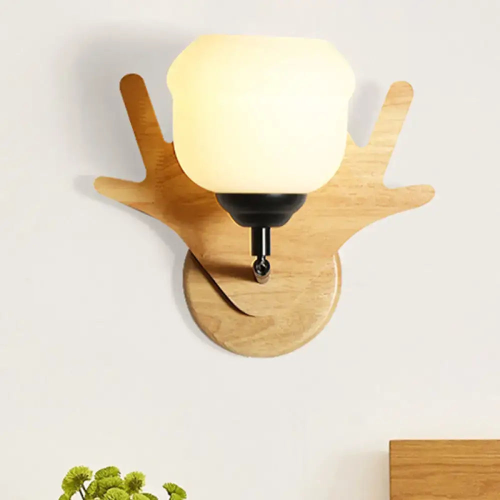A modern beige wood deer head wall light with a warm glowing frosted glass shade and antler-shaped wooden base