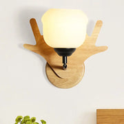 A modern beige wood deer head wall light with a warm glowing frosted glass shade and antler-shaped wooden base