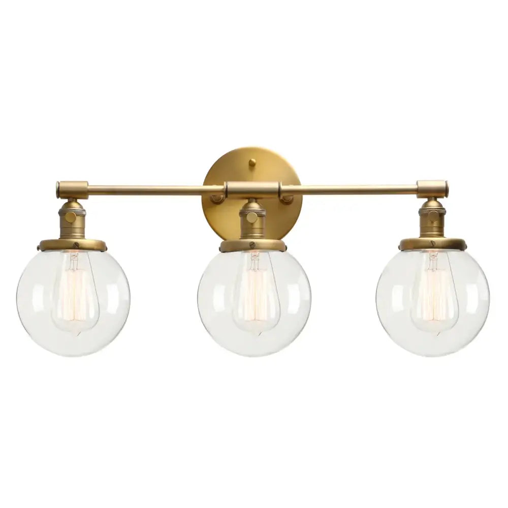 Brass-finished three-light wall sconce bathroom vanity fixture with clear glass globes and exposed filament bulbs