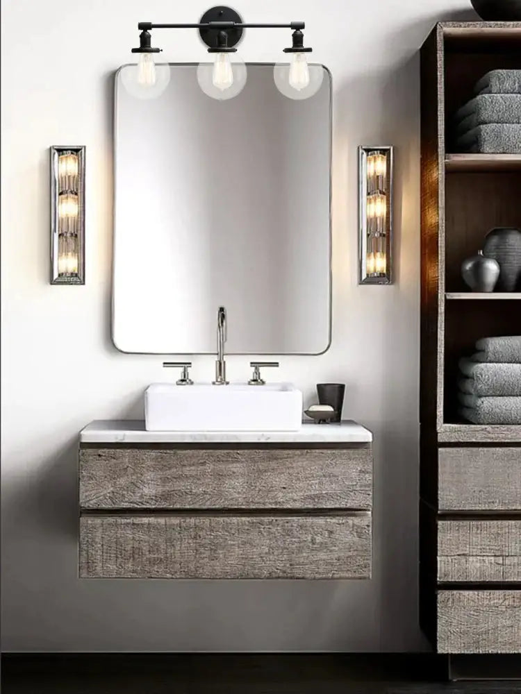 Modern black 3-light glass globe wall sconce bathroom fixture above gray wood-grain vanity with white sink and chrome faucets