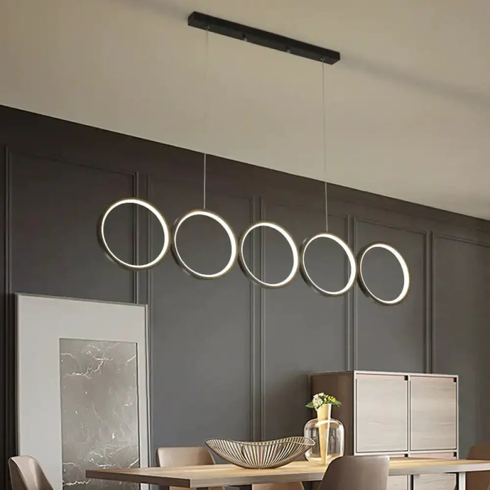 Modern black metal pendant light features five illuminated circular LED rings in a row for hanging island light use