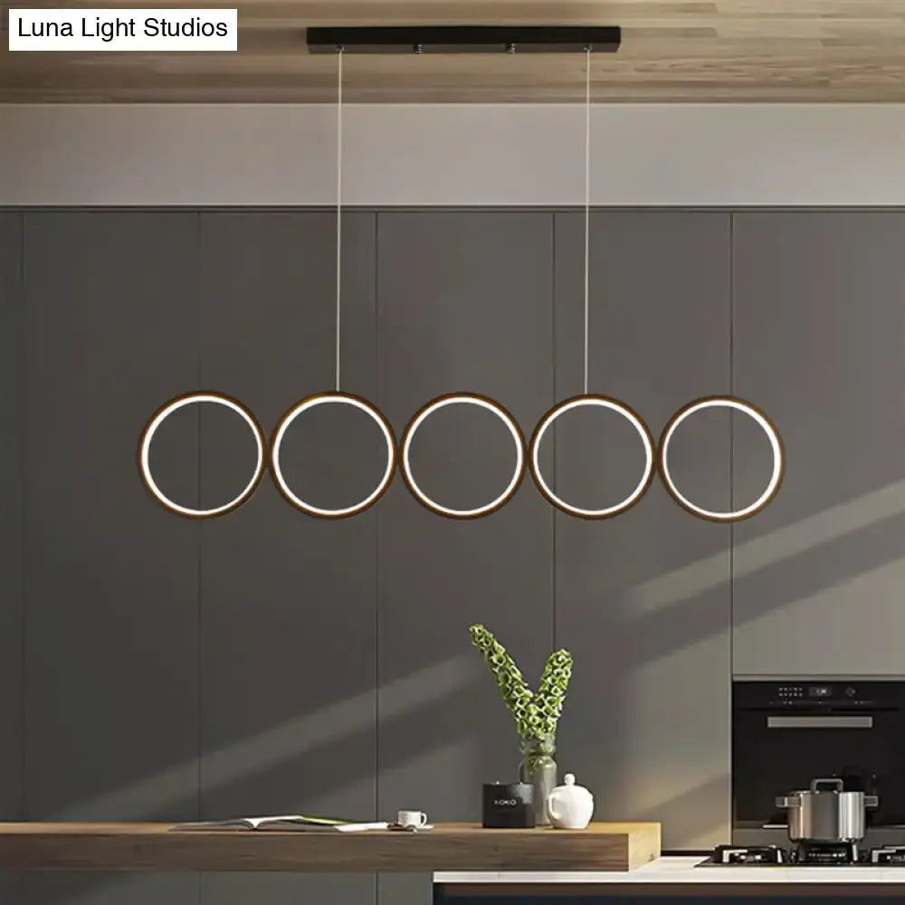 Modern black metal pendant light with five illuminated rings hanging by cords for use as a black hanging island light