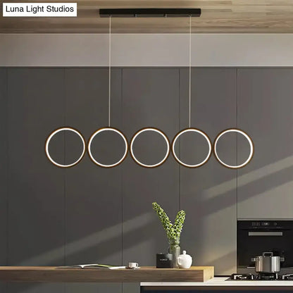 Modern black metal pendant light with five illuminated rings hanging by cords for use as a black hanging island light