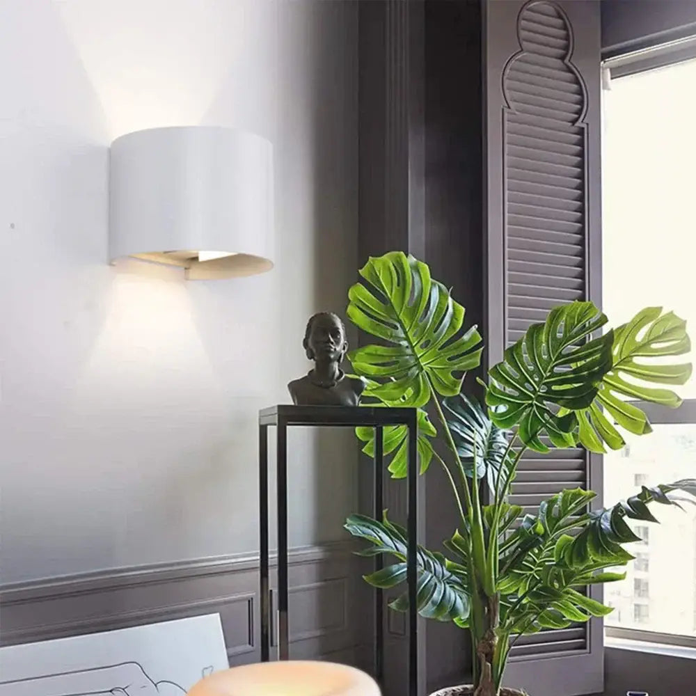 A lush green monstera plant beside a modern black decorbites adjustable aluminum wall sconce in a bedroom setting