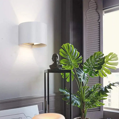 A lush green monstera plant beside a modern black decorbites adjustable aluminum wall sconce in a bedroom setting