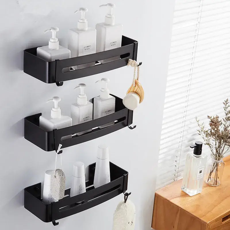 Modern black aluminum bathroom corner shelf with three tiers holding white pump bottles and hooks for bath accessories