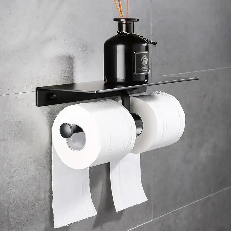 Modern black aluminum double toilet paper holder with shelf mounted on wall holding two white rolls of toilet paper