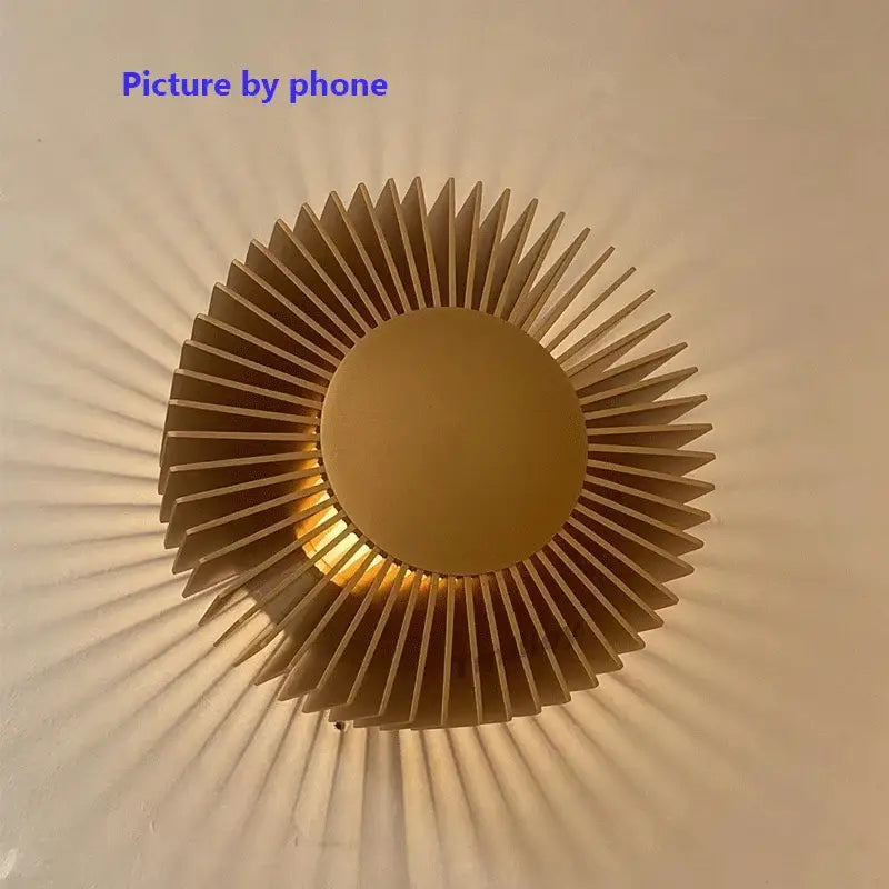 Modern black aluminum wall sconce with golden sunburst design and warm glowing center for elegant living room lighting