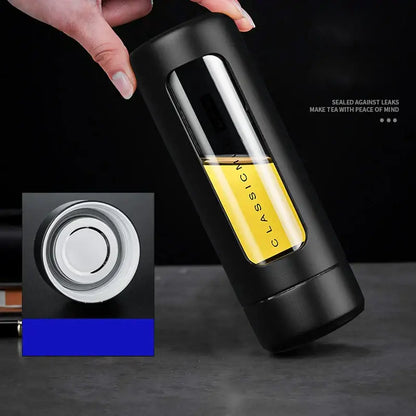Modern black and amber insulated glass water bottle with transparent window showing yellow liquid and silver lid for travel