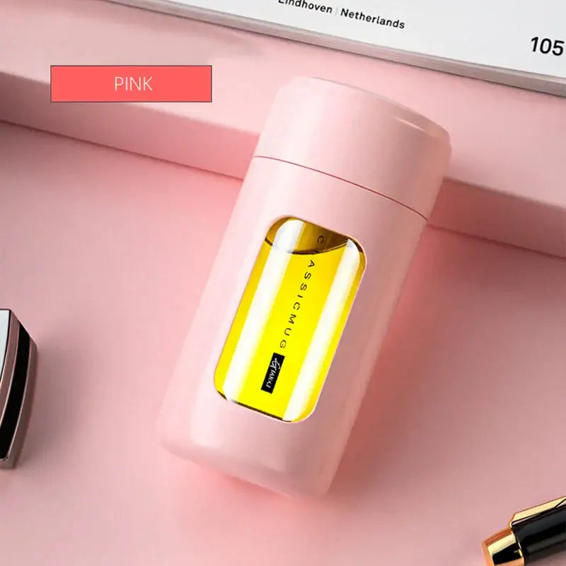 Pink cylindrical perfume bottle with transparent window showing golden-yellow liquid beside modern black and amber insulated glass water bottle