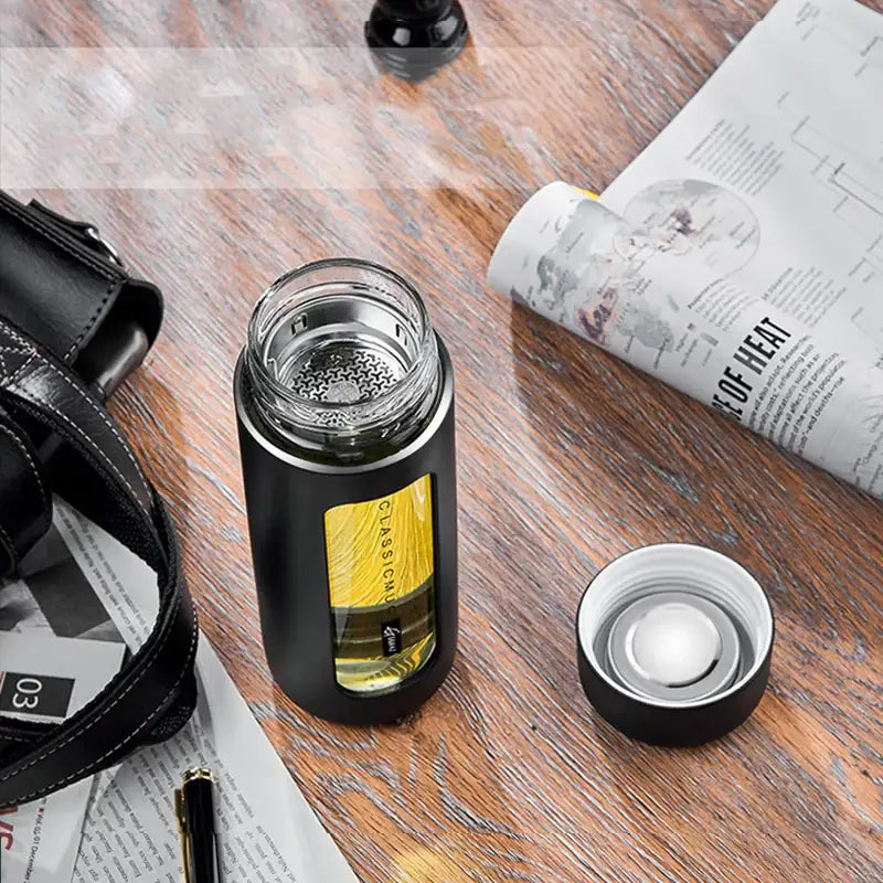 Modern black and amber insulated glass water bottle with clear glass body silver lid and yellow classic label for travel use