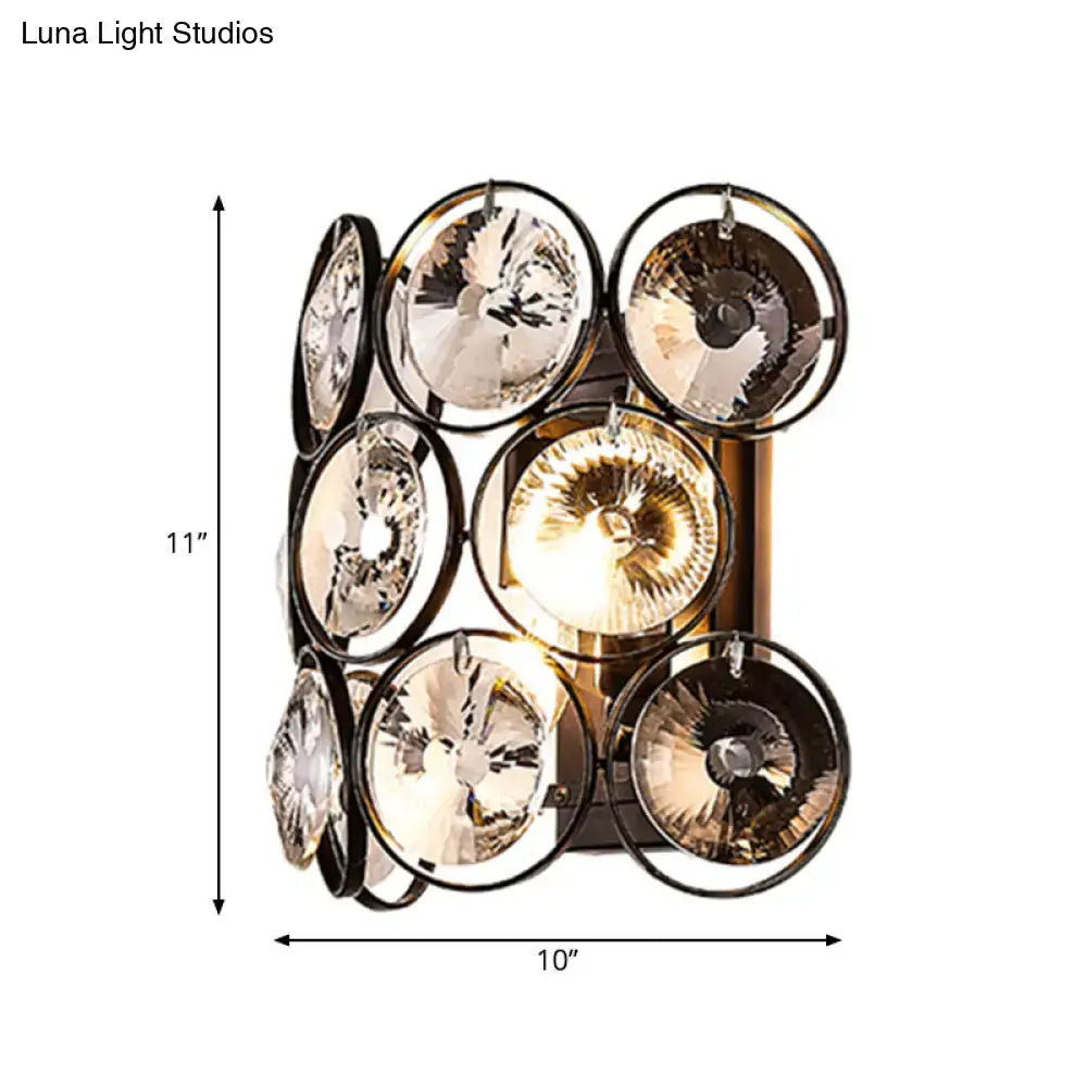 A modern black and brass wall mount light with eight faceted crystal shades on a sleek metal frame for bedroom use