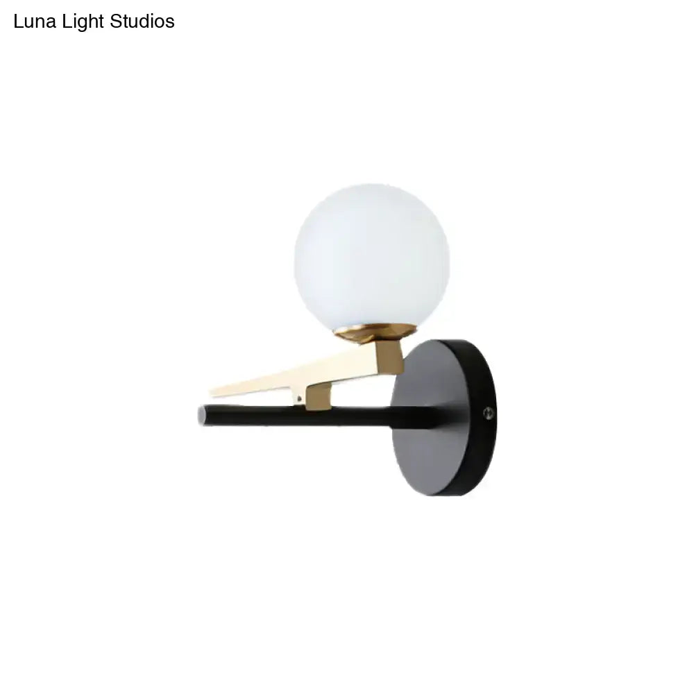 Modern black and brass wall sconce with a white glass ball shade and frosted glass globe for bedroom lighting