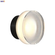 Modern black and clear acrylic wall sconce light with round ribbed glass diffuser emitting warm light for bedroom use