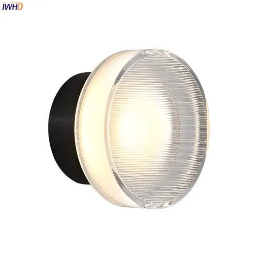 Modern black and clear acrylic wall sconce light with round ribbed glass diffuser emitting warm light for bedroom use