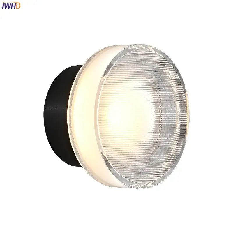 Modern black and clear acrylic wall sconce light with round ribbed glass diffuser emitting warm light for bedroom use