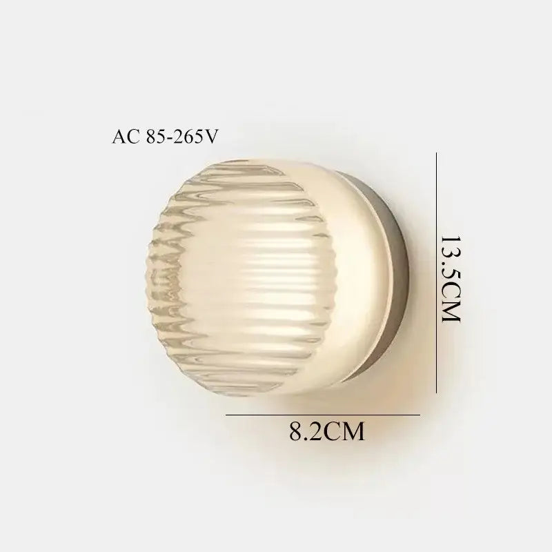 Modern wall sconce light featuring a cream-colored ribbed glass shade with a metallic base for stylish bedroom lighting