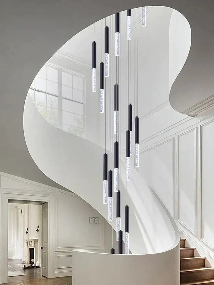 Modern black and clear glass decorbites cylindrical chandelier hanging above a curved staircase in cascading arrangement