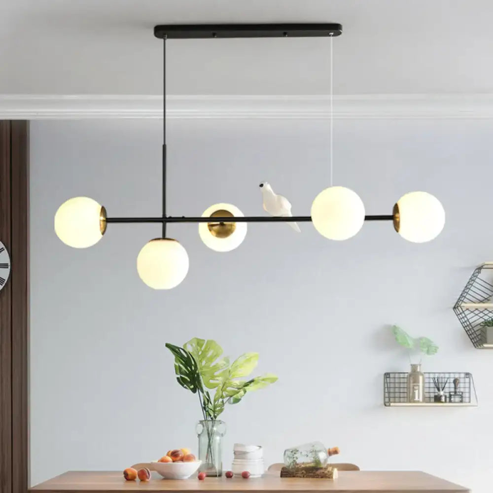 Modern black metal pendant light with five frosted glass shades and gold-toned brass sphere for island lighting