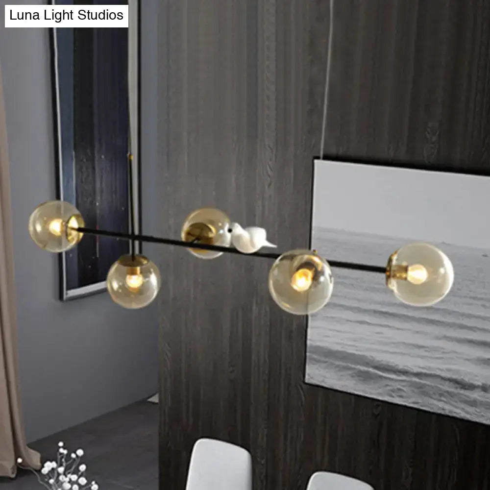 Modern minimalist pendant light with five amber glass shades and a white ceramic bird on black metal island pendant bar