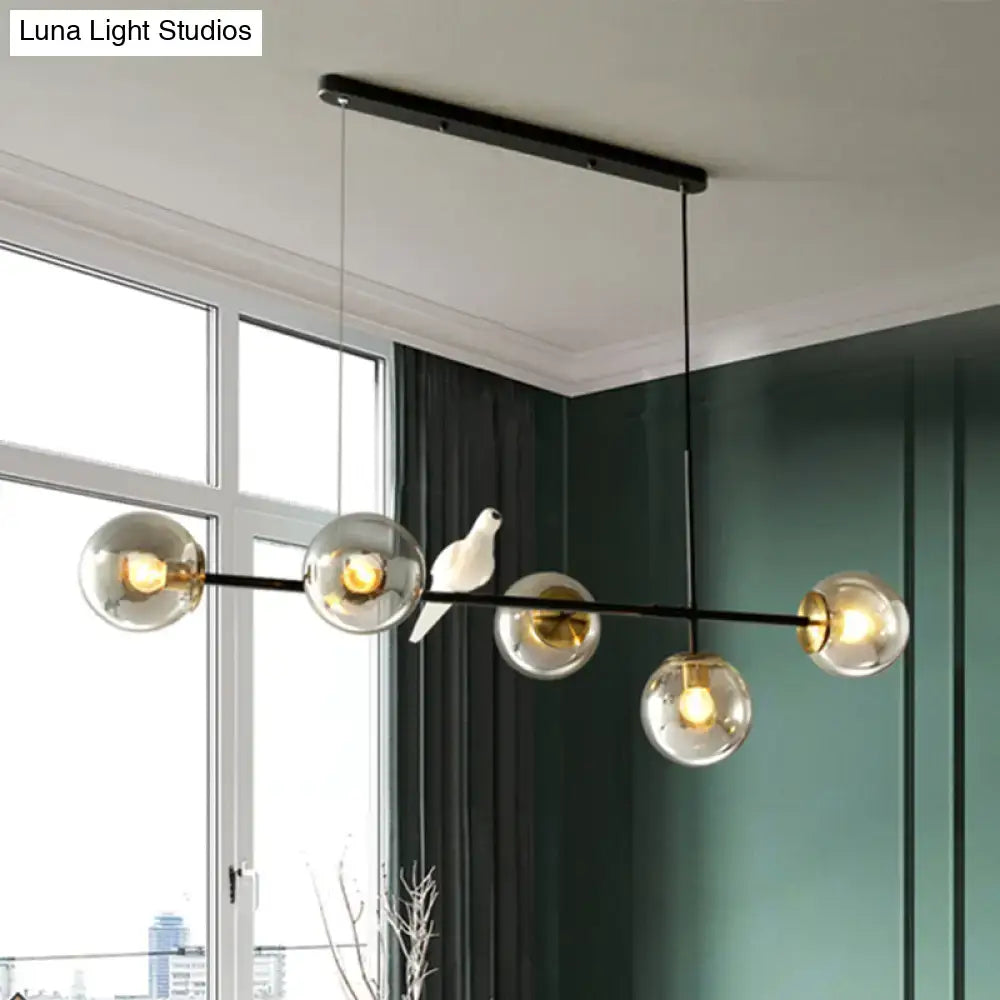 Modern black metal pendant light with five clear glass shades and white ceramic bird on central bar for island use