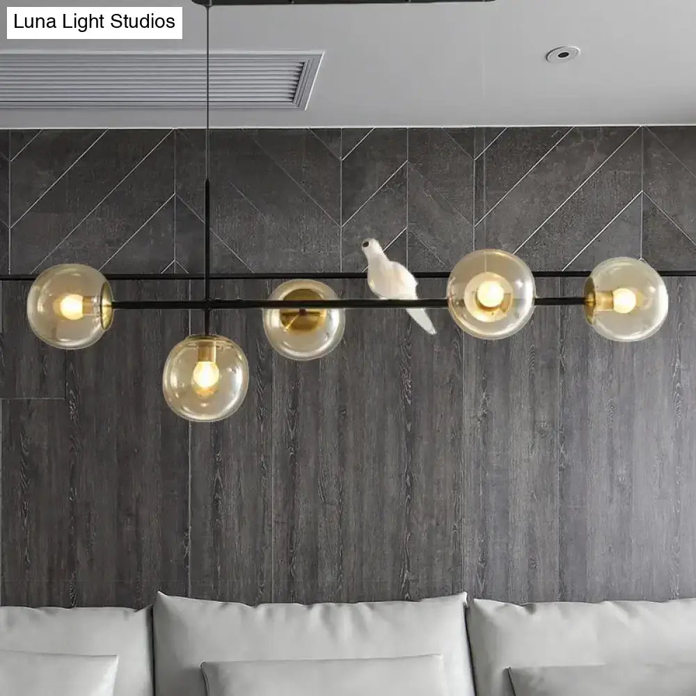 Modern black metal pendant light with five amber glass shades and a white ceramic bird on central bar for island pendant use