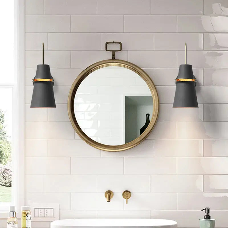 Round brass-framed mirror with vintage-style handle complementing modern black and gold conical dining room sconce