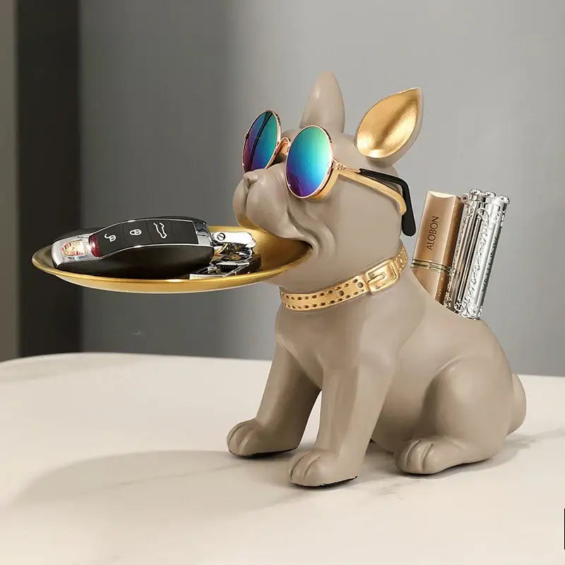 A stylish beige decorbites bulldog statue with gold accents and reflective sunglasses holds a tray for keys and cosmetics