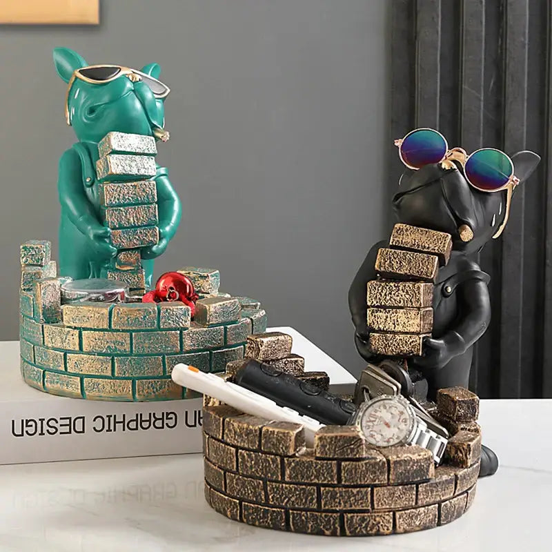 Two stylized teal and black decorbites dog statue resin figurines with sunglasses and brick stacks on their backs