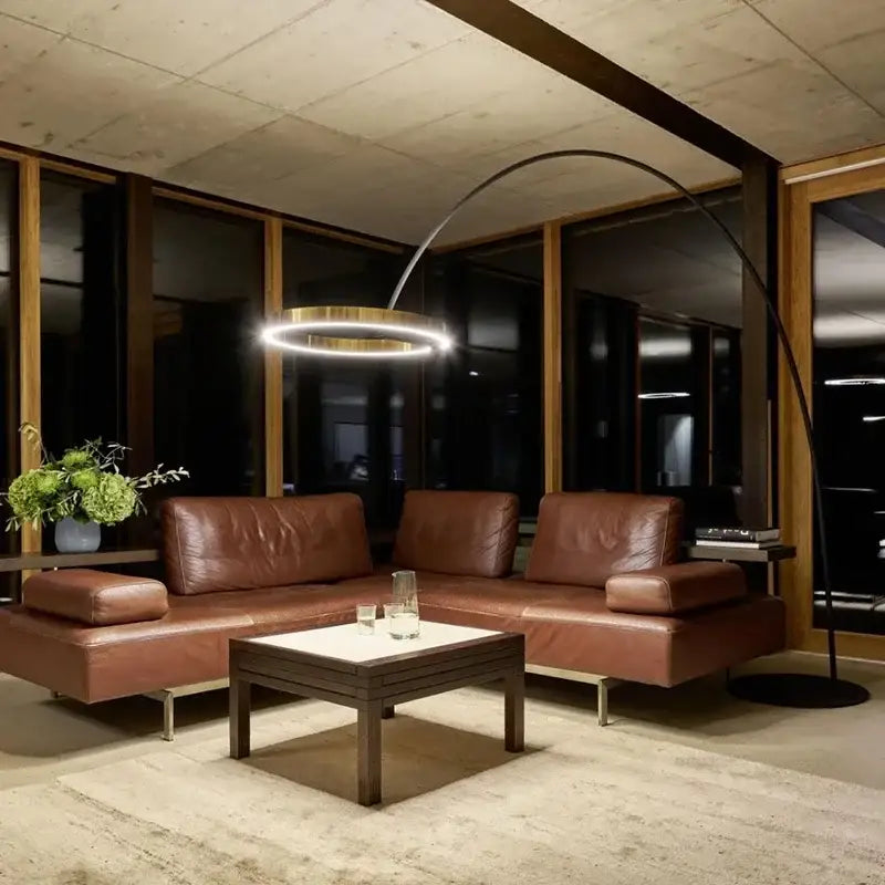 Brown leather sectional sofa with minimalist design and integrated armrests beside modern black and gold led floor lamp