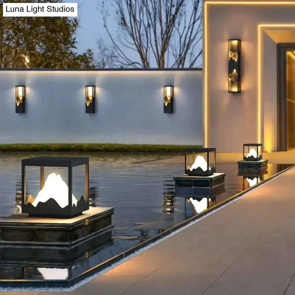 Modern black and gold cube solar led outdoor light with illuminated mountain design floating on reflective water surface