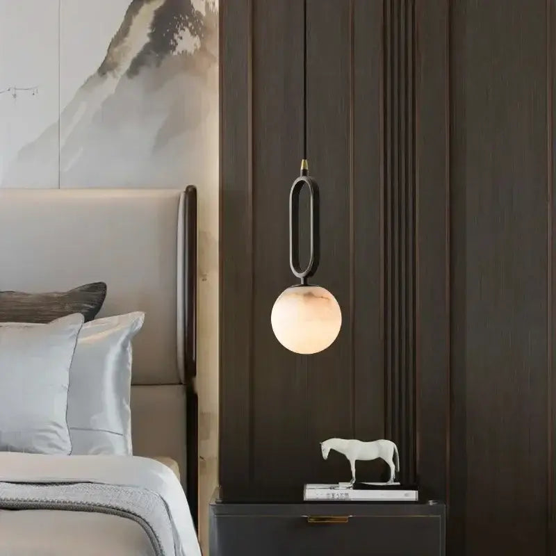 Modern pendant light with sleek black metal frame and polished copper finish featuring a warm globe shade