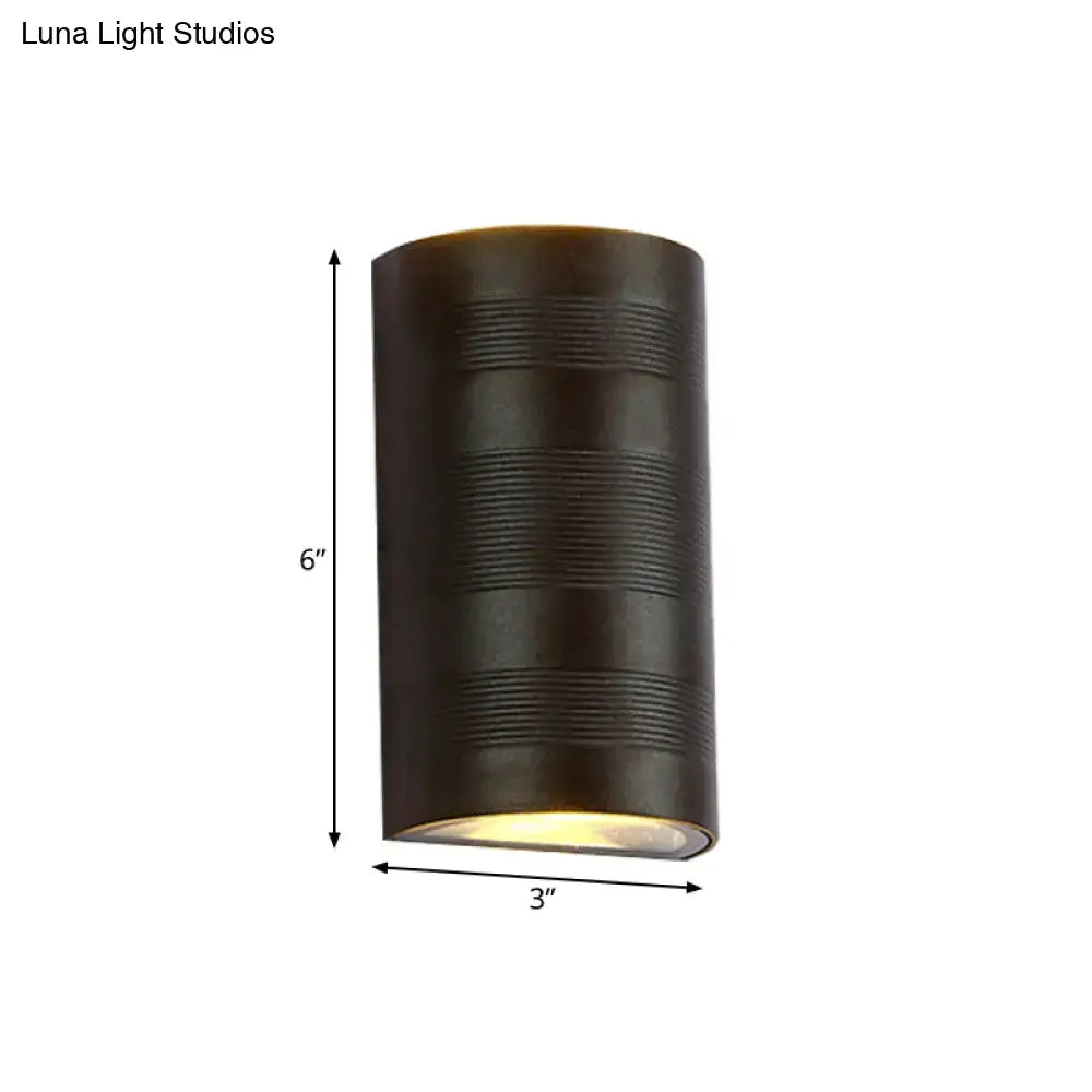 Dark bronze cylindrical outdoor wall lamp with horizontal ribbed texture and warm white light from the bottom