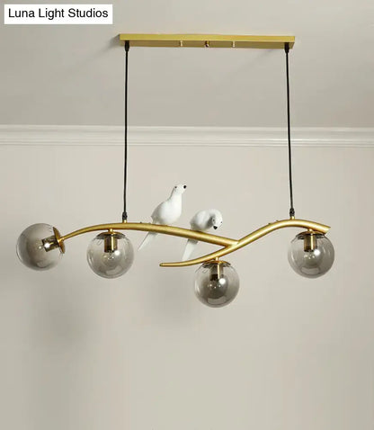 Modern pendant light with gold-toned curved branch design, smoked glass shades, and white bird figurines for linear island use