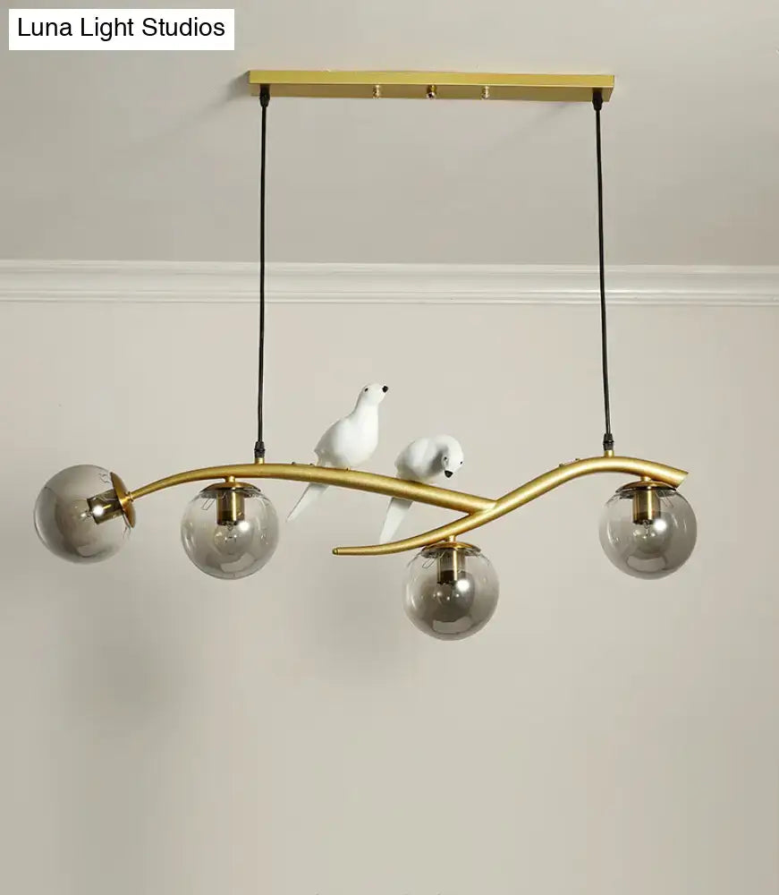 Modern pendant light with gold-toned curved branch design, smoked glass shades, and white bird figurines for linear island use