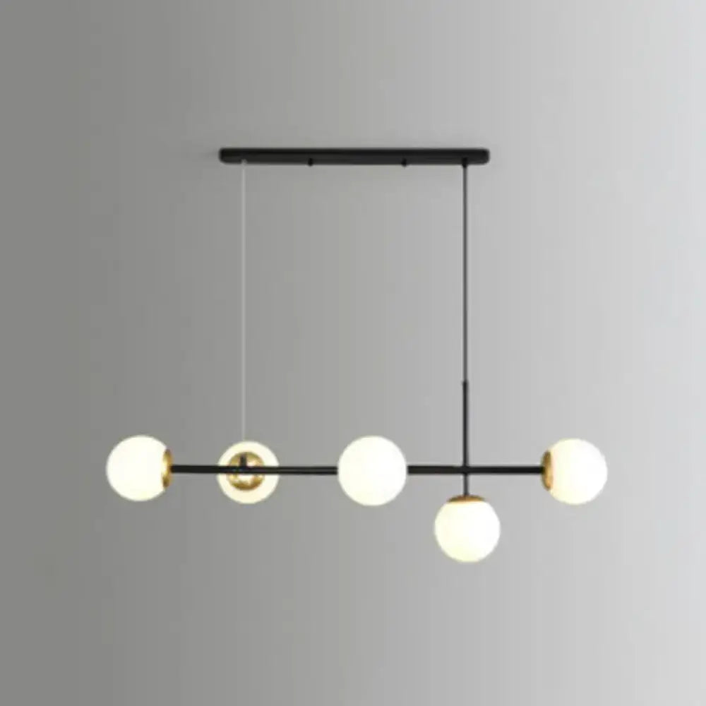 Modern black and brass pendant light with five frosted glass globe shades for linear island dining room use