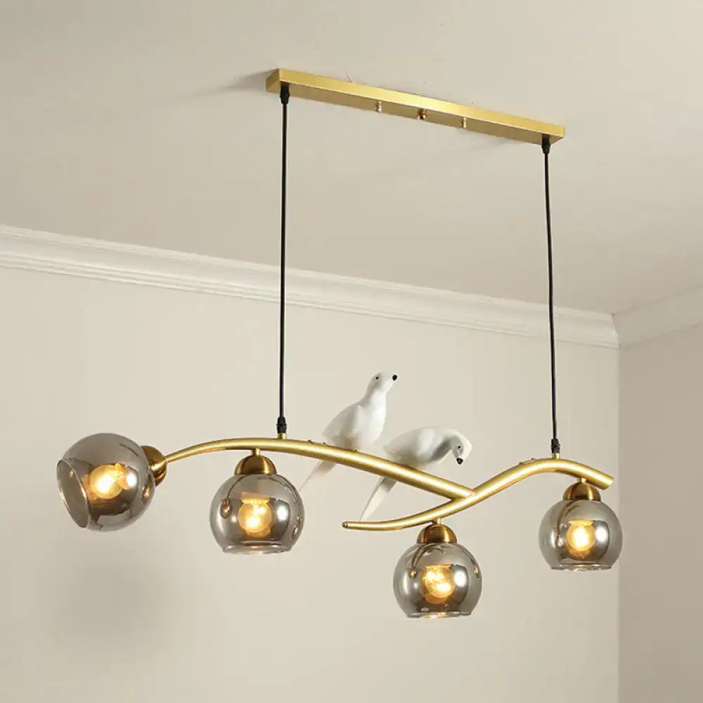 Modern black and white bird linear island pendant light with gold-toned frame and three spherical smoked glass shades