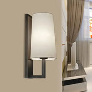 Modern black wall lamp with a cylindrical white fabric shade for bedroom lighting and contemporary decor