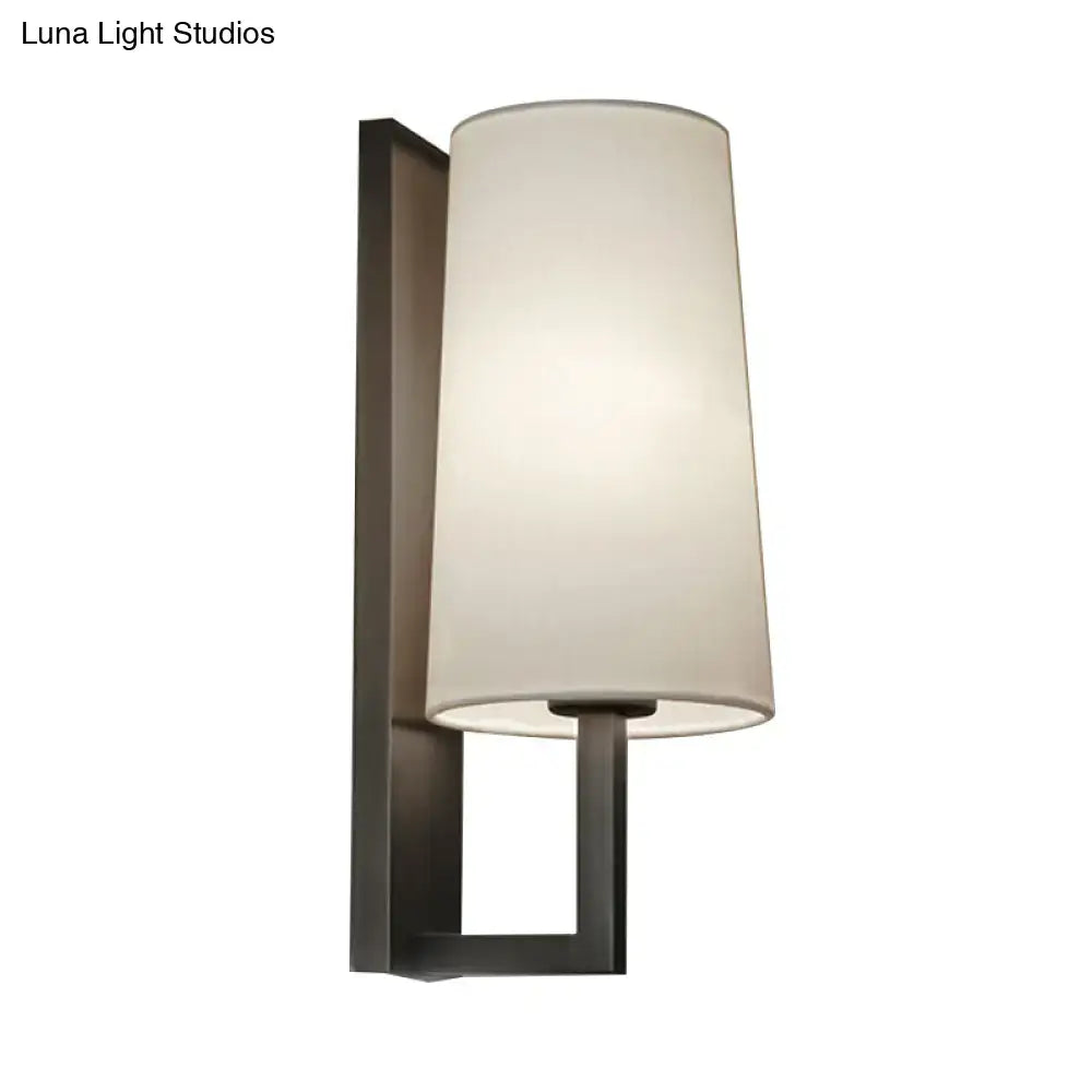 Modern black and white fabric wall lamp with a matte black metal frame and off-white cylindrical shade for bedroom lighting