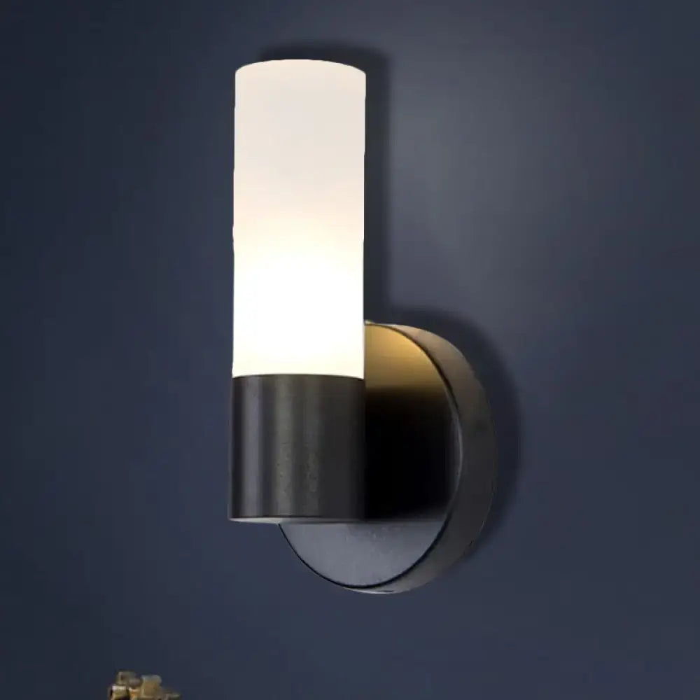 Modern black and white glass sconce lamp with cylinder white glass diffuser emitting warm bedroom wall light