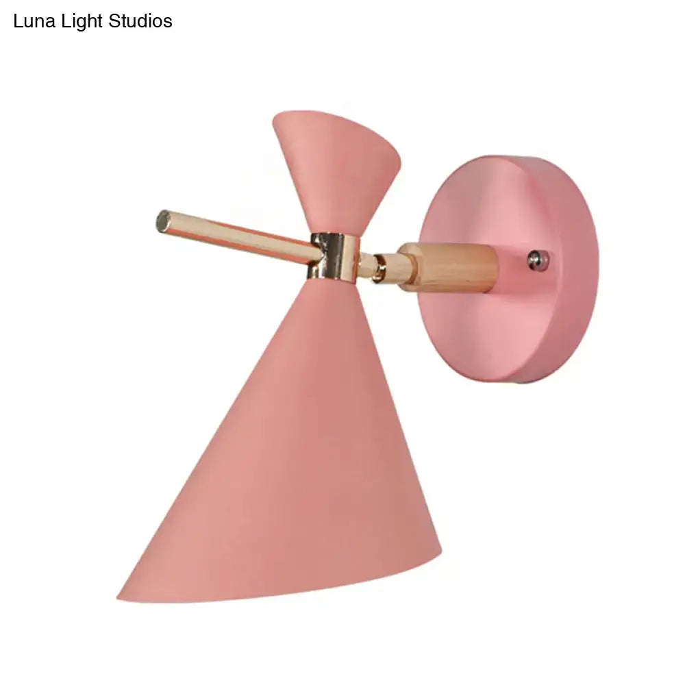 Pastel pink conical wall sconce with wooden arm and brass hardware featuring modern black angle shade design for bedroom lighting