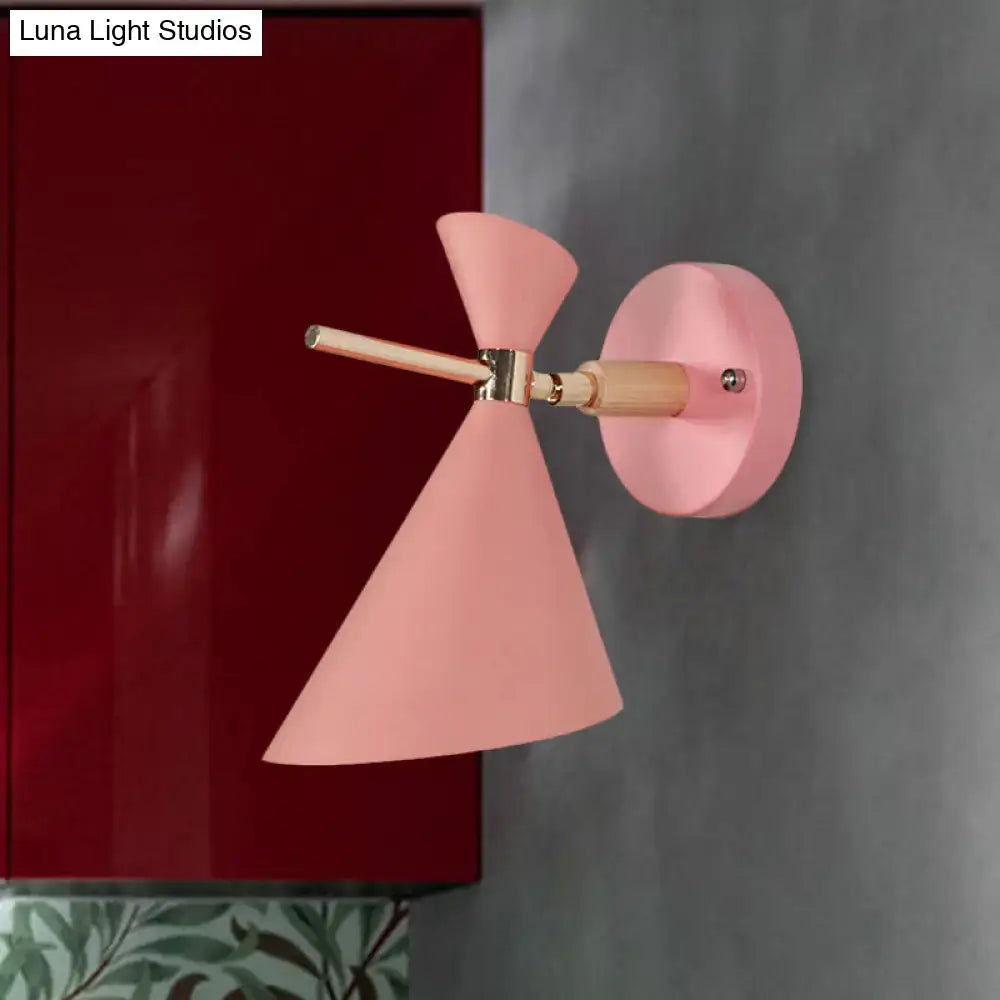 Pastel pink conical wall sconce with wooden arm and brass hardware featuring modern angle shade design for bedroom lighting