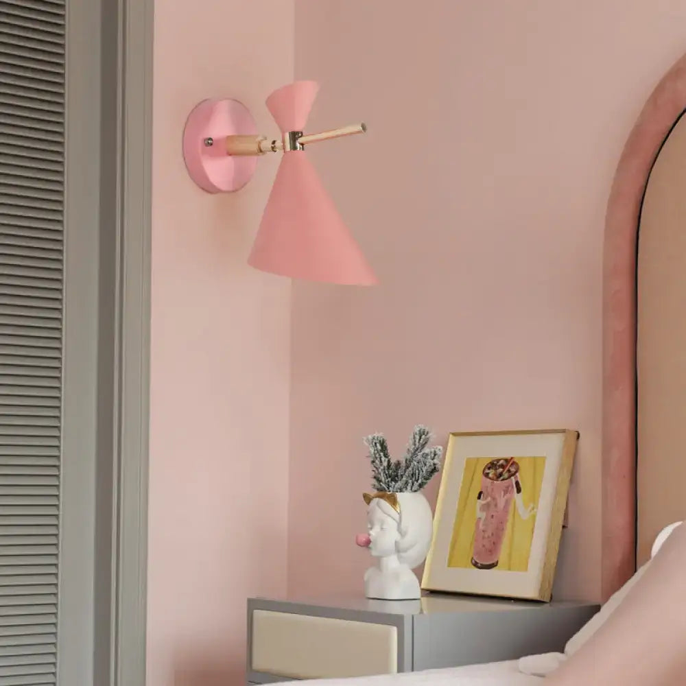 Pink conical wall sconce with wooden arm and metallic hardware featuring modern black angle shade for bedroom lighting