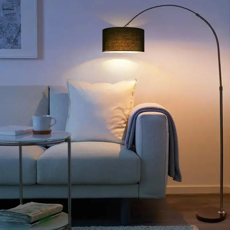 Modern black arched led floor lamp with fabric shade casting warm light over sofa in living room setting