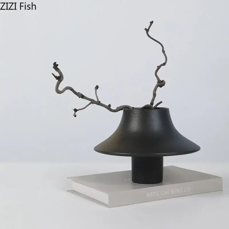Black decorbites ceramic vase with flared bell-shaped top and slender stem holding dark twisted branches for desktop decor