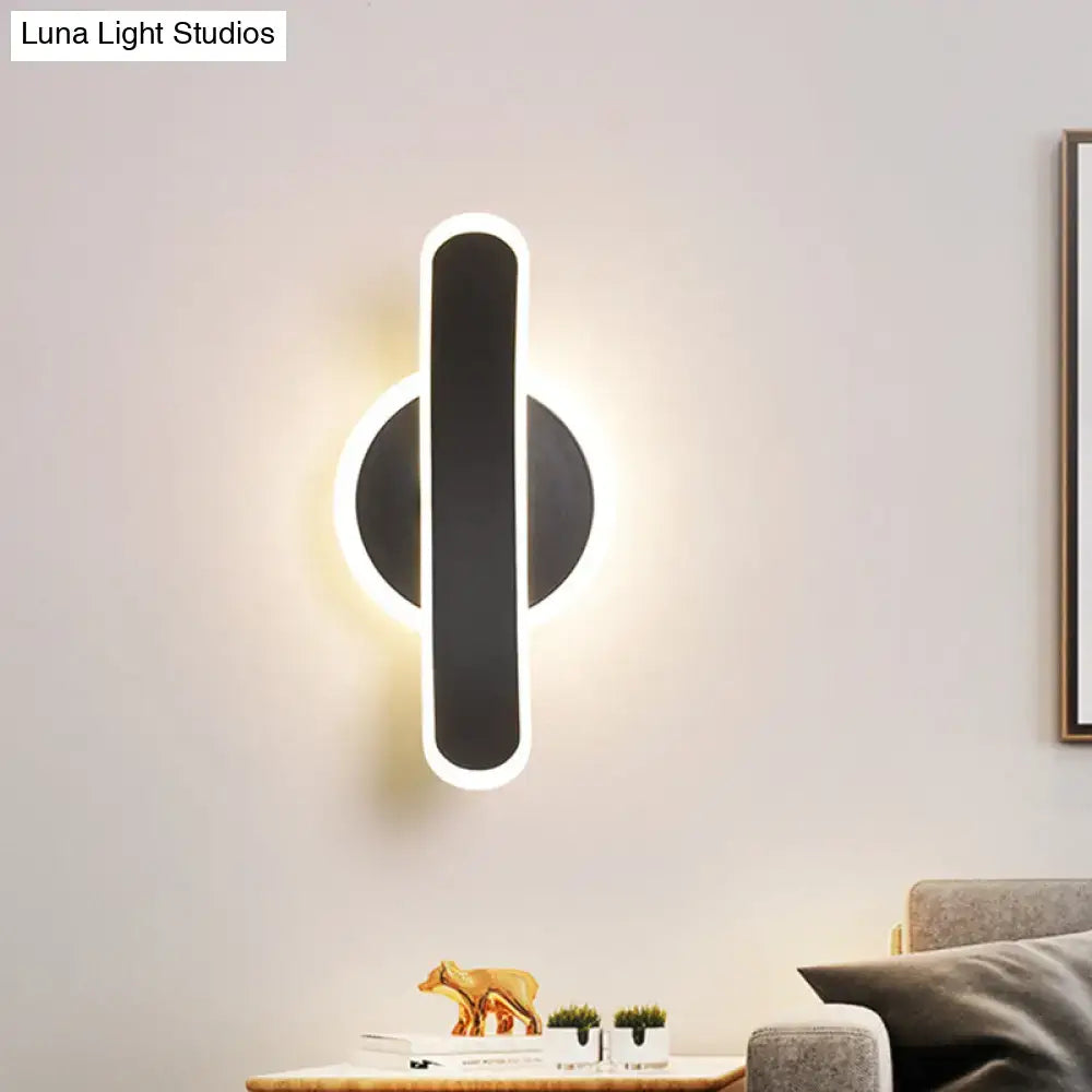 Modern black wall mounted lamp with sleek vertical bar and circular base illuminated by white warm light