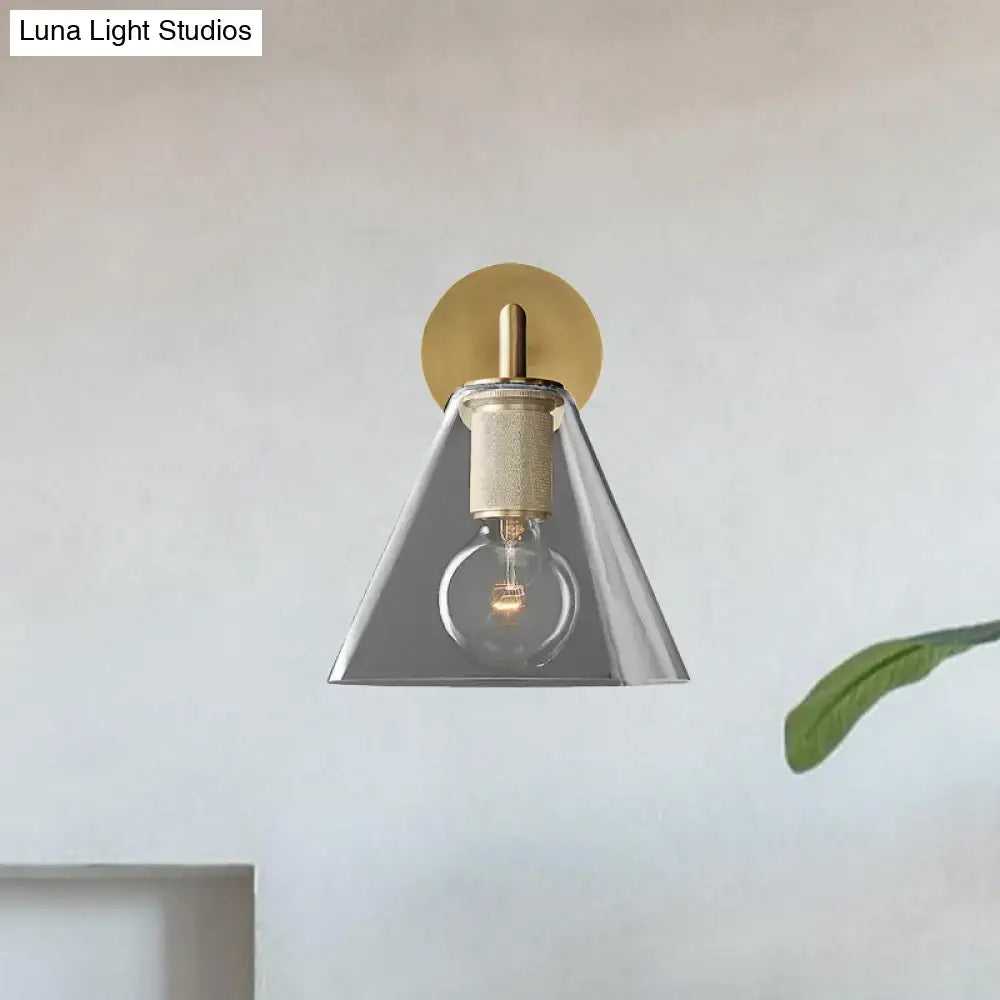 A modern wall light with brass circular backplate, clear glass cone shade, and direct wired electric edison bulb